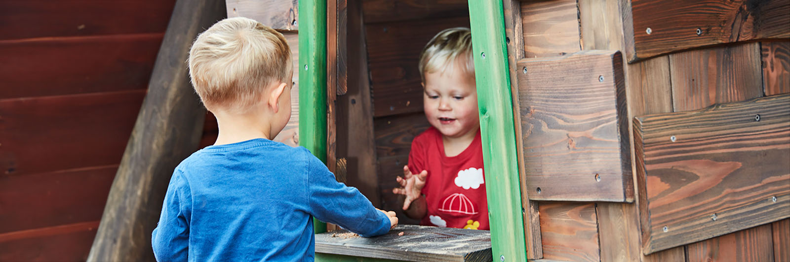 Two boys playing kiosk on a wooden playhouse.